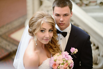 Wedding couple indoors is hugging each other. Beautiful model girl in white dress. Man in suit. Beauty bride with groom. Female and male portrait. Woman with lace veil. Cute lady and handsome guy