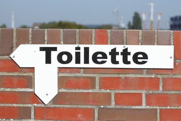 Toilettenschild mit Pfeil auf einer Ziegelmauer