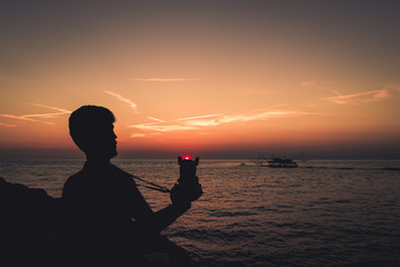 Fototapeta premium Silhouette di un ragazzo giovane che tiene in mano una macchina fotografica al tramonto.