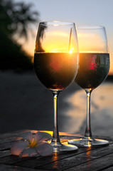 Romantic beach scene: two glasses of red wine at sunset near water