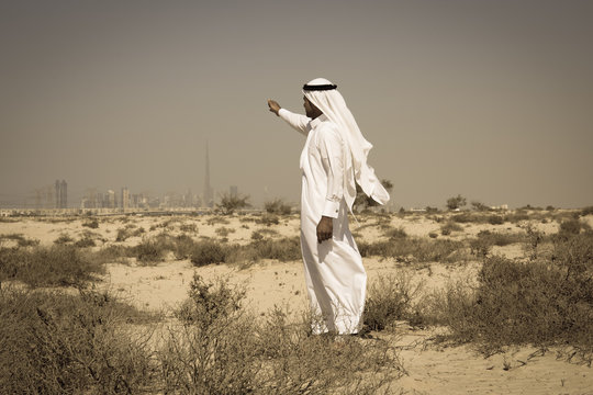 Arab man in national dress stands in the desert and looks at the