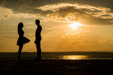 silhouette Romantic couple lovers standing facing each other at colorful sea side sunset on...