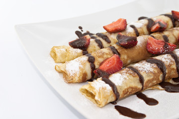 Sweet dessert of rolled pancakes on a plate with strawberry 