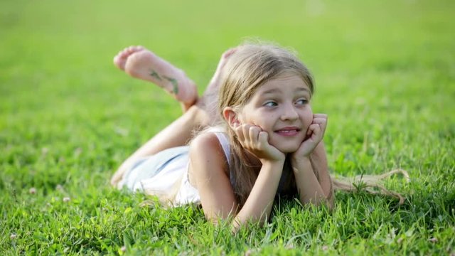 glad small girl in elementary school age lying on green grass in park