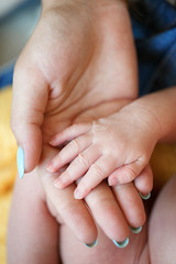 Newborn baby put his little hand on the palm of his gentle mother,the mother's nails are painted blue nail Polish,the baby and mother are sitting on soft yellow blanket