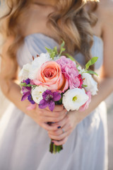 Obraz na płótnie Canvas Beautiful wedding bouquet of assorted colors of white,pink,lilac and red flowers in hands of bride dressed in wedding dress,curly blond hair accentuated a bouquet of flowers
