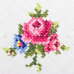 Rose motiv hand embroidery on white linen tablecloth.  Multicolored cross stich decoration with...