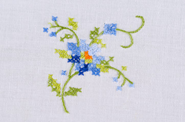 Blue flower motiv hand embroidery on white linen tablecloth.  Multicolored cross stich decoration with yarn. Handicraft. Macro photo close up from above.