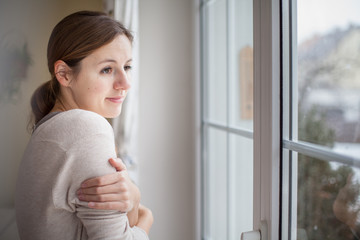 Woman looking from a window of her house on a cold and snowy win
