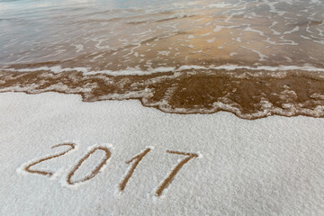 2017, message written on the sand at the snow beach background