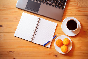 Overhead view of  notebook, laptop, fresh cakes and a white cup of coffee