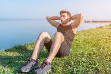 Sporty young man doing sit-ups abs crunches in nature.