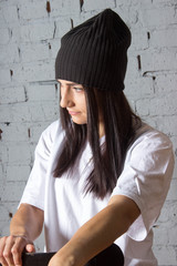 Портрет европейской девушки на фоне кирпичной стены в футболке и в шапке