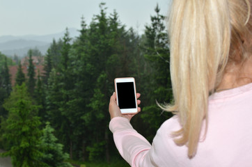Blonde woman with ponytail looking at landscape and her black cell phone screen suitable for copy text or picture