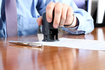 Close-up Of Businessman Hand Pressing a  Stamp On Document in th