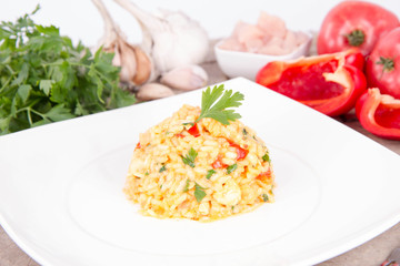 Risotto with chicken, tomatoes, bell pepper, onion, parsley and garlic on a white plate on a wooden background
