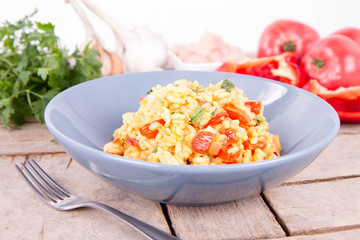 Risotto with chicken, tomatoes, bell pepper, onion, parsley and garlic on a blue plate on a wooden background