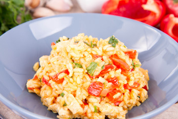 Risotto with chicken, tomatoes, bell pepper, onion, parsley and garlic on a blue plate on a wooden background