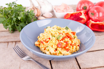 Risotto with chicken, tomatoes, bell pepper, onion, parsley and garlic on a blue plate on a wooden background