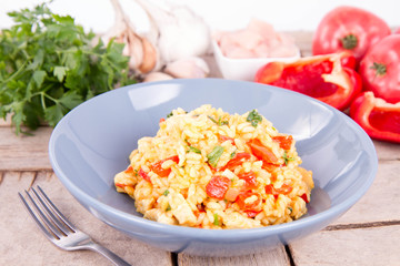 Risotto with chicken, tomatoes, bell pepper, onion, parsley and garlic on a blue plate on a wooden background