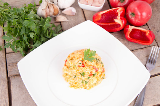 Risotto with chicken, tomatoes, bell pepper, onion, parsley and garlic on a white plate on a wooden background