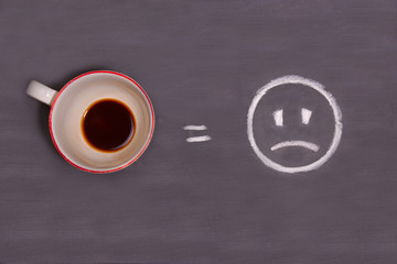 Obraz na płótnie Canvas A cup of coffee and sad smiley drawn with chalk on the table. Energy from coffee.