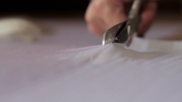 Close up of hands with scissors cutting white material
