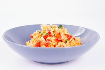 Risotto with chicken, tomatoes, bell pepper, onion, parsley and garlic on a blue plate on a wooden background
