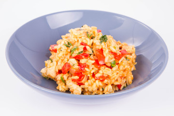 Risotto with chicken, tomatoes, bell pepper, onion, parsley and garlic on a blue plate on a wooden background