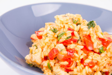 Risotto with chicken, tomatoes, bell pepper, onion, parsley and garlic on a blue plate on a wooden background