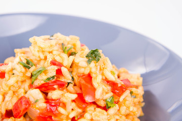 Risotto with chicken, tomatoes, bell pepper, onion, parsley and garlic on a blue plate on a wooden background