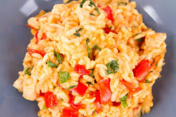Risotto with chicken, tomatoes, bell pepper, onion, parsley and garlic on a blue plate on a wooden background