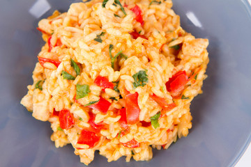 Risotto with chicken, tomatoes, bell pepper, onion, parsley and garlic on a blue plate on a wooden background