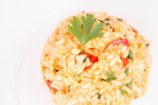 Risotto with chicken, tomatoes, bell pepper, onion and garlic on a white plate decorated with parsley