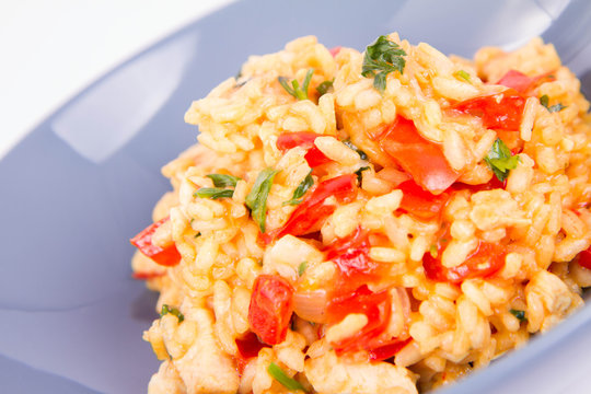 Risotto with chicken, tomatoes, bell pepper, onion, parsley and garlic on a blue plate on a wooden background