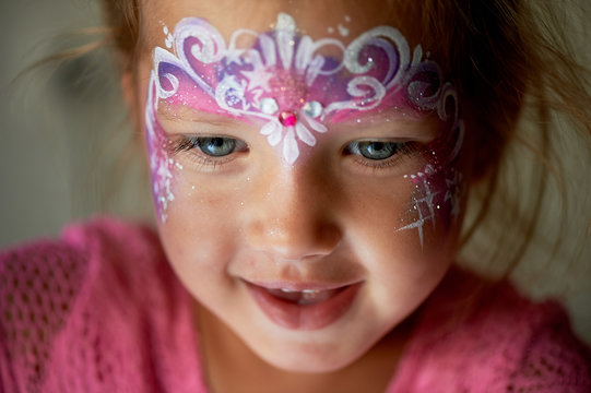 Pretty exciting blue-eyed girl of 2 years with a pink face painting