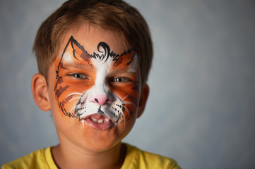 6 years old boy with blue eyes with face painting of a cat or a tiger. Orange.