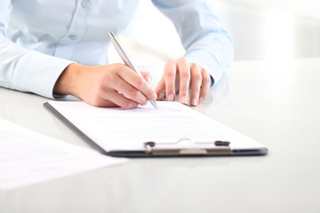 Woman's hands writing on sheet of paper in a clipboard and a pen