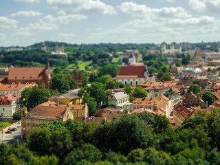 Daytime tilt and shift view of Latvia houses and their sunny roofs among green trees under blue...