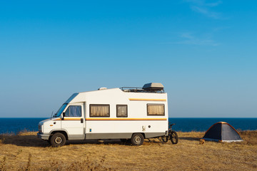 Camper parked on the beach on blue sky background
