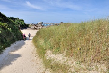 Un couple de randonneurs descent un sentier de dunes vers la plage de Trégastel en Bretagne