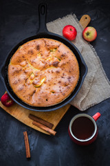 Homemade apple pie in vintage iron pan tea and apples on dark background.