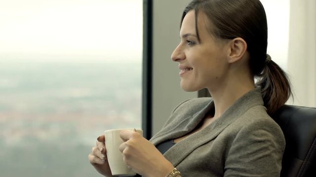 Happy woman drinking coffee while sitting on chair by window at home
