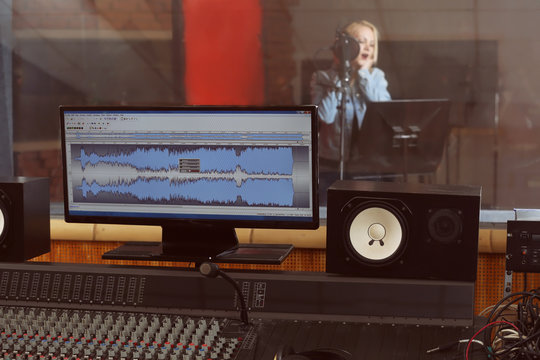 Young woman recording a song in a professional studio. View from sound engineer workplace
