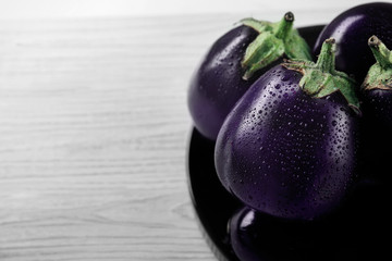 Plate with fresh aubergines on wooden background