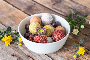 Colorful dessert, raw vegan sweets and organic chocolate in a bowl on a wooden background decorated with chrysanthemum flowers for autumn mood 