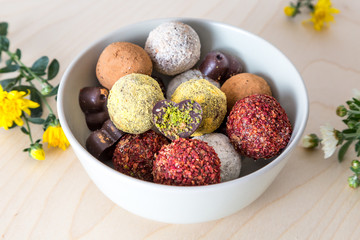Colorful dessert, raw vegan sweets and organic chocolate in a bowl on a wooden background decorated with chrysanthemum flowers for autumn mood 