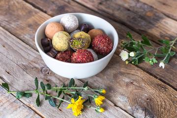 Colorful dessert, raw vegan sweets and organic chocolate in a bowl on a wooden background decorated with chrysanthemum flowers for autumn mood 