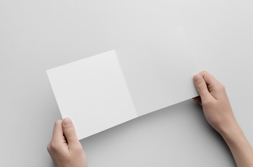 Square Bi-Fold Brochure Mock-Up - Male hands holding a blank bi-fold on a gray background.