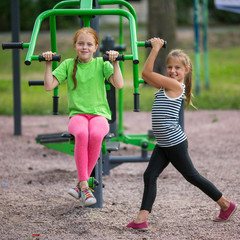 Fototapeta na wymiar Two little girls is engaged in sport fitness equipment on the Playground.